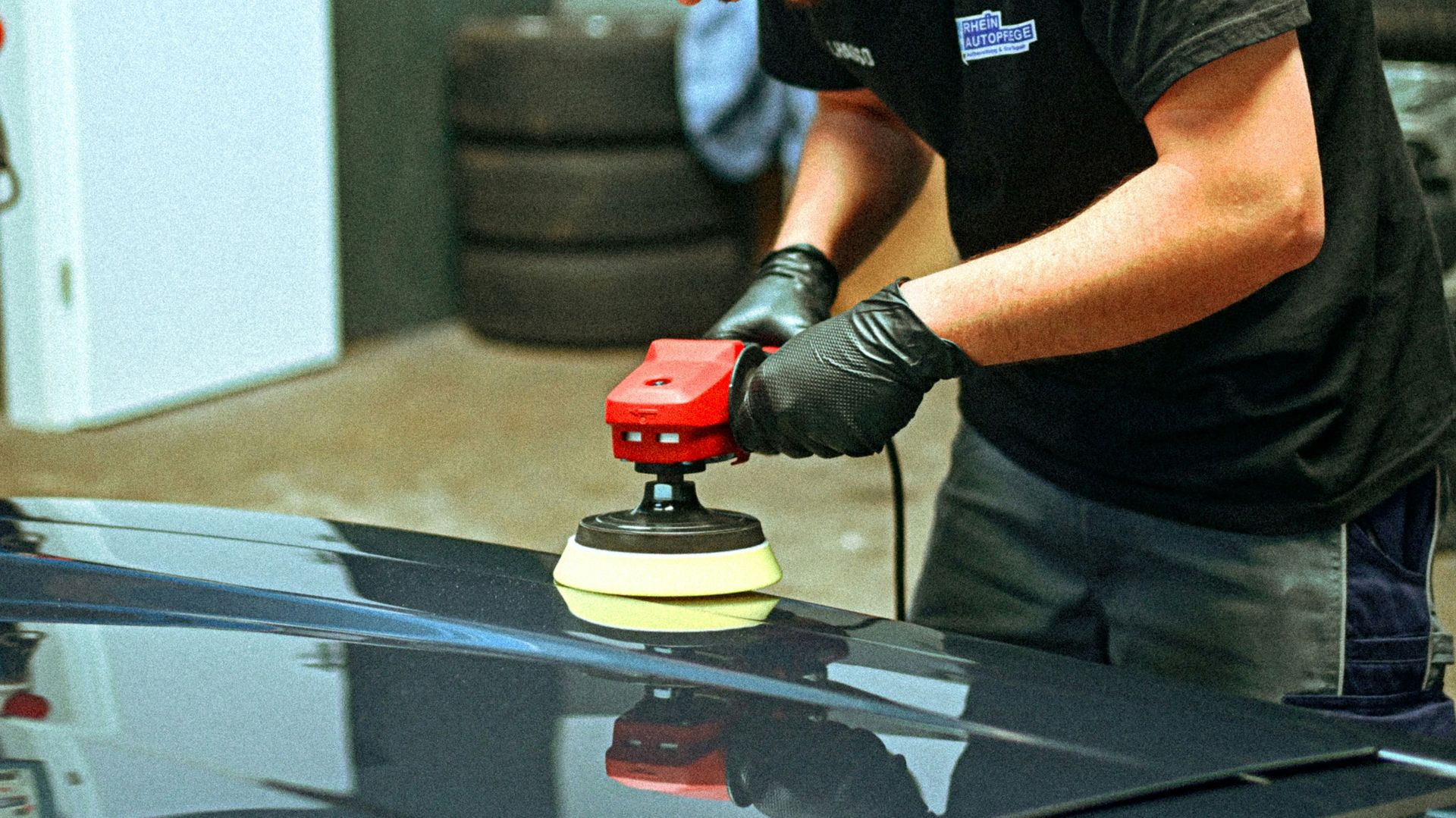 A person polishes a dark car with an electric polisher